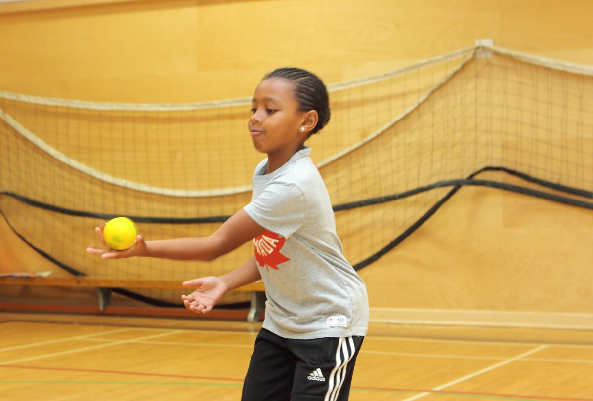 young girl catching a yellow ball with one hand